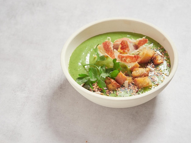 Tigela de sopa verde com sementes de salsa de presunto e pão torrado por cima como enfeite