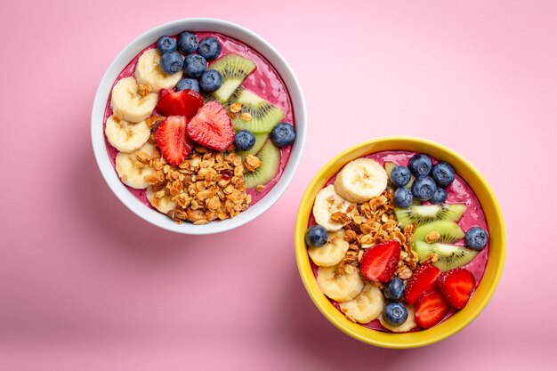 Tigela de suco de açaí de verão com morangos, banana, mirtilos, kiwis e granola em fundo rosa pastel. taça de café da manhã com frutas e cereais, close-up, vista de cima, comida saudável