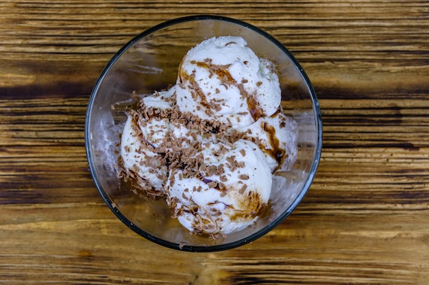 Tigela de vidro com bolas de sorvete e cobertura de chocolate em uma mesa de madeira Vista superior