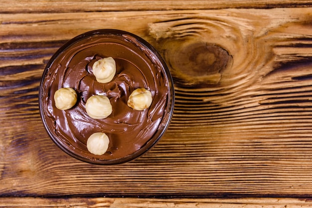 Tigela de vidro com chocolate e avelãs em uma mesa de madeira vista superior