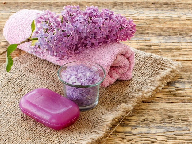 Tigela de vidro com flores lilás de sabão de sal marinho e toalha para procedimentos de banheiro em pano de saco