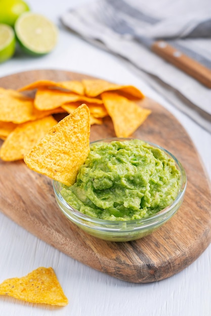 Tigela de vidro com molho de guacamole mexicano saudável feito de abacate servido com nachos na mesa