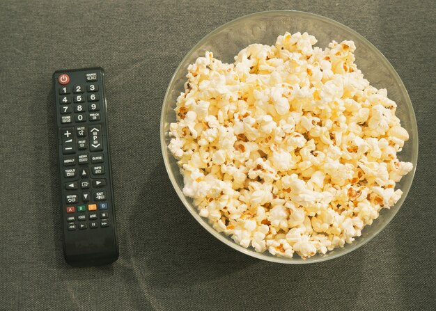 tigela de vidro com pipoca e controle remoto da TV no sofá