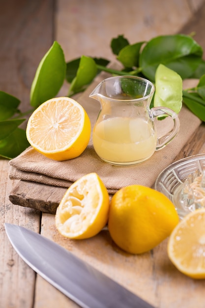 tigela de vidro de suco de limão espremido na hora, espremedor de limão e limões maduros em fundo de madeira