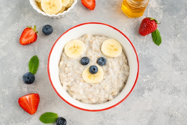 Tigela divertida com mingau de aveia com caras de urso feita de frutas e bagas Idéia de comida para crianças