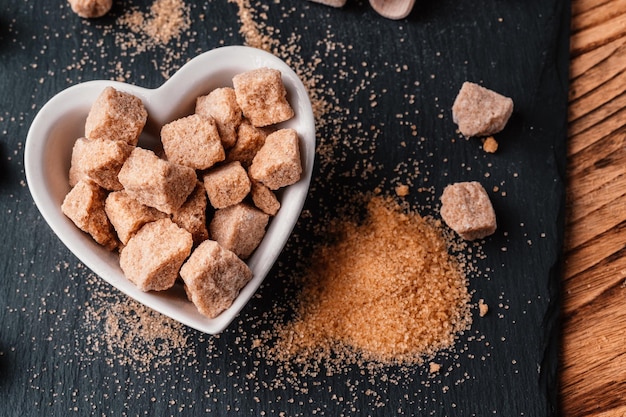 Tigela e colher com areia e açúcar mascavo no fundo de madeira cubo de açúcar mascavo Faça nutrição insalubre obesidade diabetes atendimento odontológico e muito mais