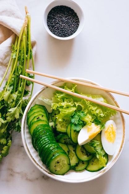 Tigela saudável, salada de pepino com ovos e coentro no fundo de mármore, vista superior