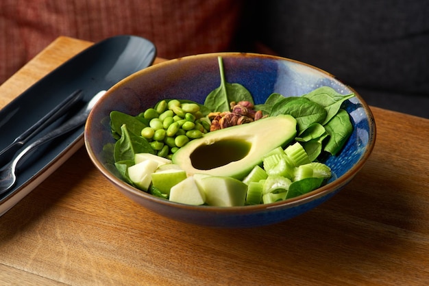 Tigela verde de tigela vegana de comida saudável com abacate e legumes verdes em um fundo de madeira