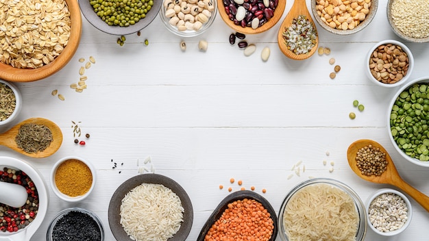 Tigelas com diferentes cereais: arroz, ervilhas, lentilhas, feijão e especiarias numa mesa de madeira branca. Postura plana. Vista do topo. Copie o espaço.