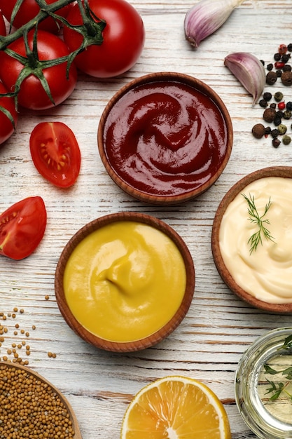 Tigelas com maionese de ketchup de mostarda e ingredientes na mesa de madeira plana