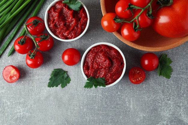 Tigelas com pasta de tomate na superfície cinza com ingredientes