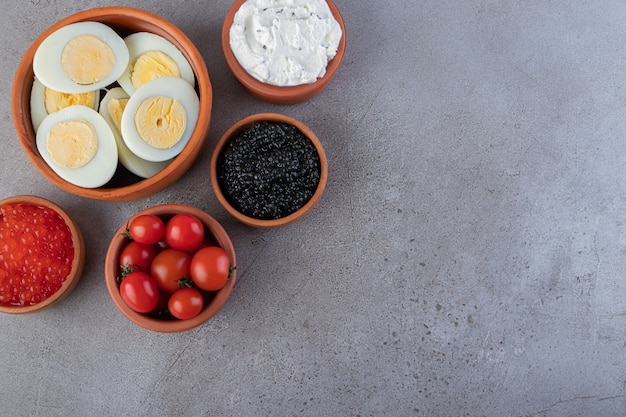 Tigelas de barro de café da manhã saudável com ovos, creme e caviar na mesa.