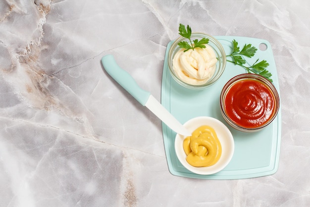 Tigelas de porcelana com ketchup mostarda e molho de queijo com folhas de salsa e uma faca