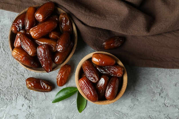 Tigelas de tâmaras secas e guardanapo de cozinha em fundo cinza texturizado