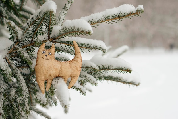 Foto tigre de juguete, gato, símbolo del horóscopo oriental 2022, con el telón de fondo de un árbol de navidad cubierto de nieve. nevando. fondo de invierno borroso. el concepto del próximo año nuevo.