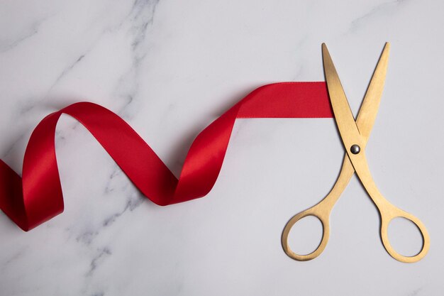 Tijeras de oro de fondo de gran apertura con cinta roja sobre un fondo de mármol