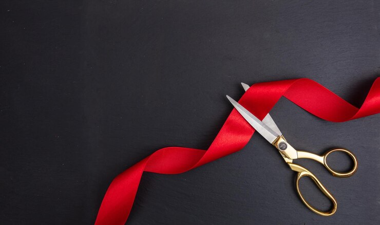 Tijeras que cortan la cinta de seda roja contra fondo negro
