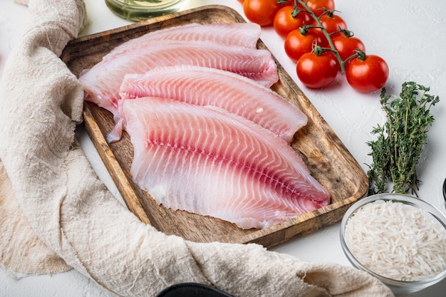 Foto tilápia de peixe branco cru, com ingredientes de arroz basmati e tomate cereja, em branco