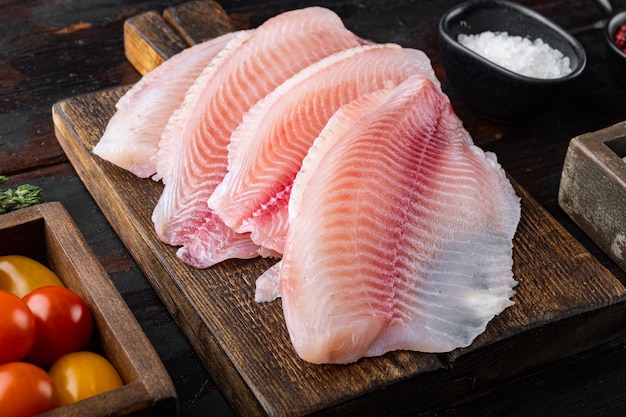 Tilápia de peixe branco cru, com ingredientes de arroz basmati e tomate cereja, em fundo escuro de madeira