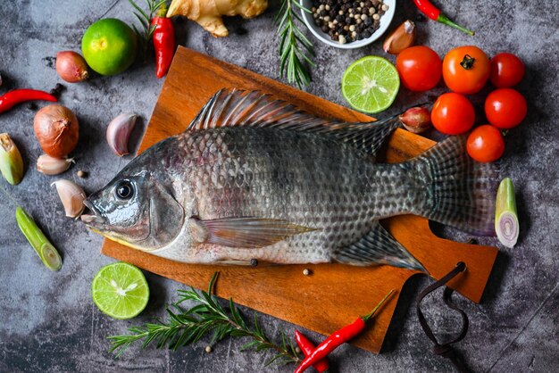 Foto tilapia con especias romero tomate limón jengibre ajo pimienta en fondo oscuro pescado de tilapia crudo fresco de la granja de tilapia