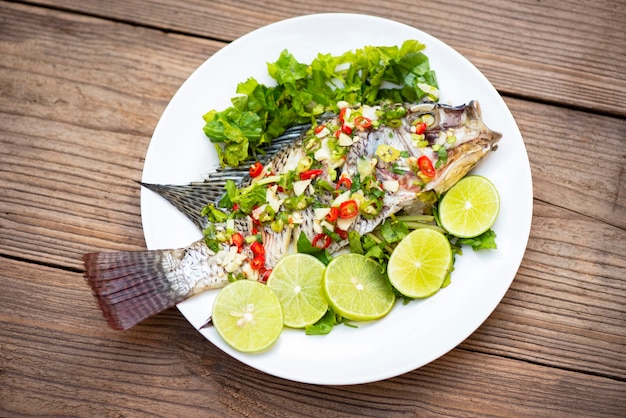 Tilápia no vapor com molho de pimenta e lima e limão com ervas e vegetais no prato, Peixe lima ao vapor - comida tailandesa