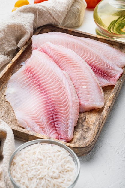 Foto tilapia de pescado blanco crudo, con arroz basmati y tomates cherry ingredientes, sobre mesa blanca