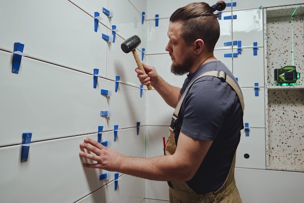 Tiler golpea las cuñas del sistema de nivelación de baldosas de cerámica de la pared del baño