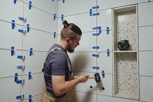 Tiler golpea las cuñas del sistema de nivelación de baldosas de cerámica de la pared del baño