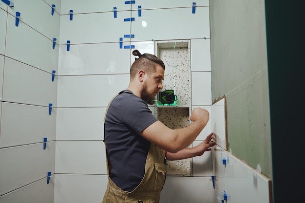 Tiler tendido instalando baldosas de cerámica en la pared del baño