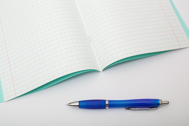 Útiles escolares aislados sobre fondo blanco. foto sobre el tema de estudiar en la escuela. Cuaderno y un bolígrafo azul sobre un fondo blanco.