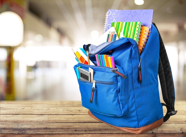 Útiles escolares coloridos en mochila sobre fondo de madera