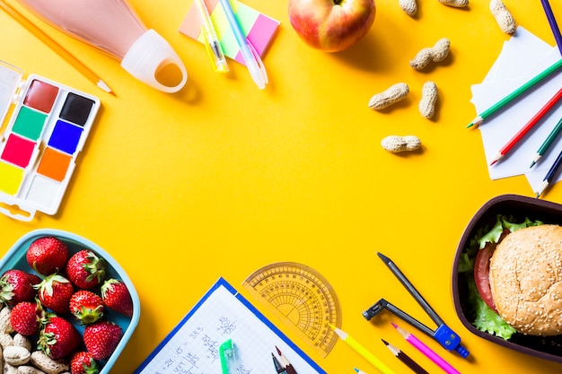 Útiles escolares del niño y almuerzo en cajas plásticas sobre fondo amarillo.