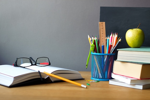 Útiles escolares, pila de libros, pizarra y libro abierto con gafas sobre una superficie de madera