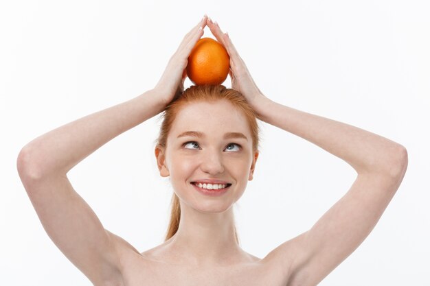 Ótima comida para um estilo de vida saudável. Mulher jovem e bonita sem camisa segurando um pedaço de laranja em pé