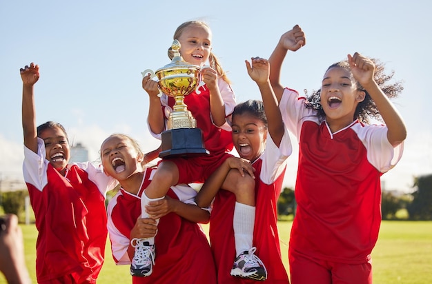 Time de futebol e troféu com crianças em comemoração juntos como um grupo vencedor de meninas para uma competição esportiva Trabalho em equipe de futebol e prêmio com jogadores de esporte comemorando o sucesso ao ar livre