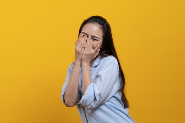 Foto tímida mulher asiática em vestido casual, cobrindo o rosto e espreitar isolado em fundo amarelo