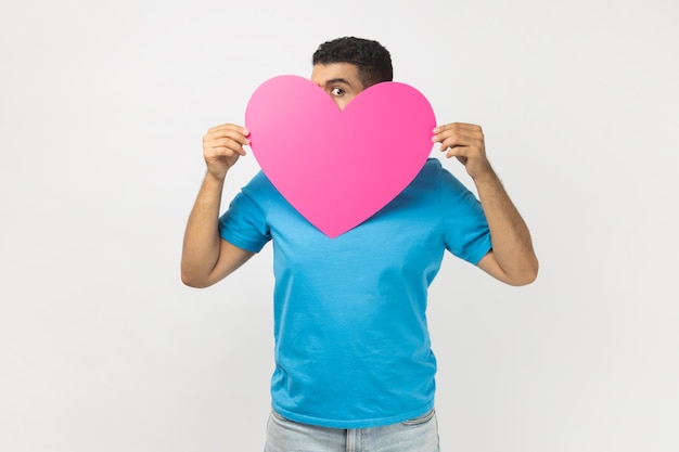 Tímido hombre anónimo asomándose desde un gran corazón rosa siendo tímido para expresar sus sentimientos el día de san valentín