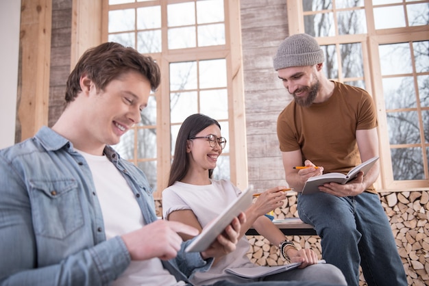 Ótimo humor. Jovens alegres e positivos sentados juntos e sorrindo enquanto apreciam a conversa