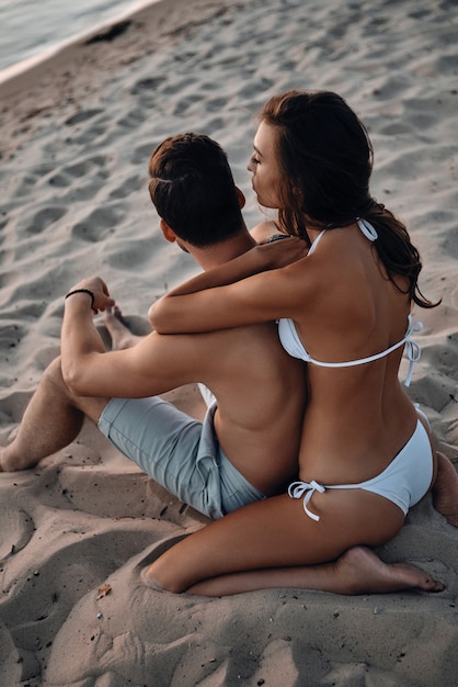 Ótimo tempo juntos. Bela jovem abraçando o namorado enquanto relaxa na praia