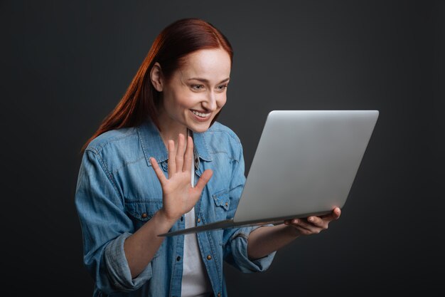 Ótimo ver você de novo. Senhora animada e comprometida encantadora fazendo uma videochamada e curtindo uma conversa enquanto usa seu laptop