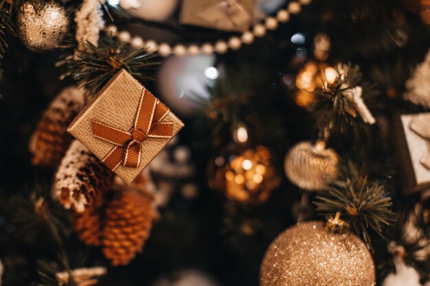 Tinny beige Weihnachtsgeschenkbox mit einem beige glänzenden Band, das am Weihnachtsbaum hängt Feiertag