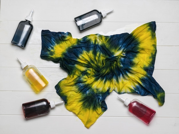 Tintas multicoloridas e uma camiseta tie dye pintada em amarelo e azul flat lay