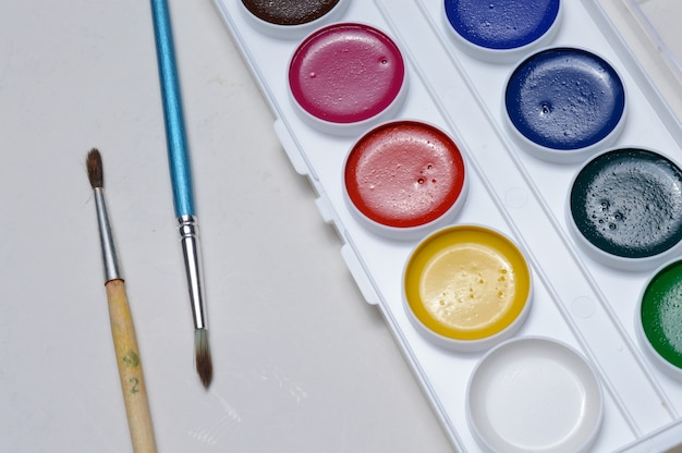 Tintas multicoloridas para desenho em paleta e pincel. em um close-up de fundo claro.