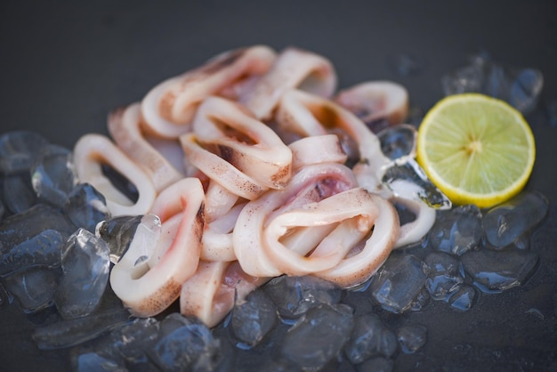 Tintenfischringe auf Eis, frischer roher Tintenfisch mit Salat-Meeresfrüchte-Zitrone auf schwarzem Plattenhintergrund