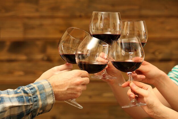 Tintineo de copas de vino tinto en las manos sobre fondo de tablones de madera rústica