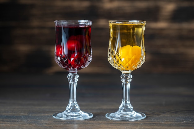 Tintura casera de cereza roja y ciruela cereza amarilla en copas de cristal de vino sobre fondo de madera