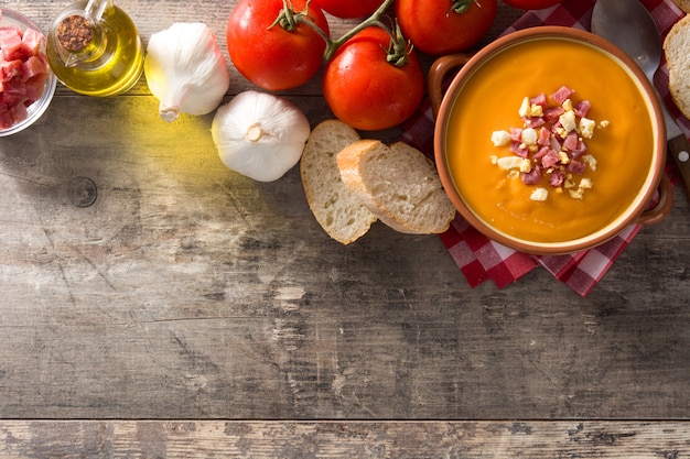 Típica crema de salmorejo español con jamón y huevo sobre mesa de madera, vista superior, espacio de copia