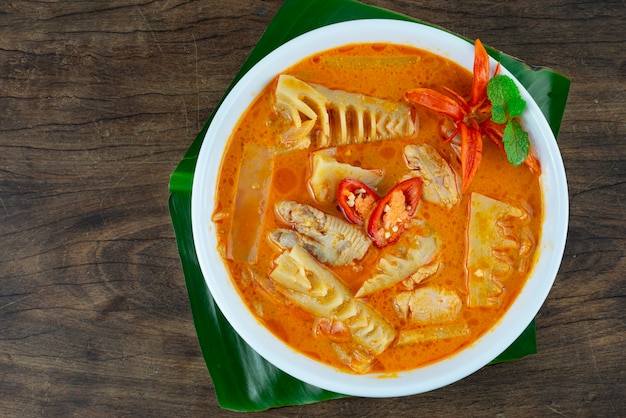 Foto típico bambú de curry rojo de tailandia con pollo y leche de coco en un recipiente sobre fondo de madera