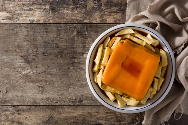 Típico sandwich francés francesinha con papas fritas en la mesa de madera