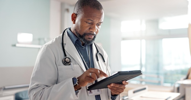 Tipo de atención médica y un hombre negro o médico con una tableta para una aplicación médica o comunicación Lectura de correo electrónico madura y un cirujano africano con tecnología para obtener información sobre resultados o consejos quirúrgicos